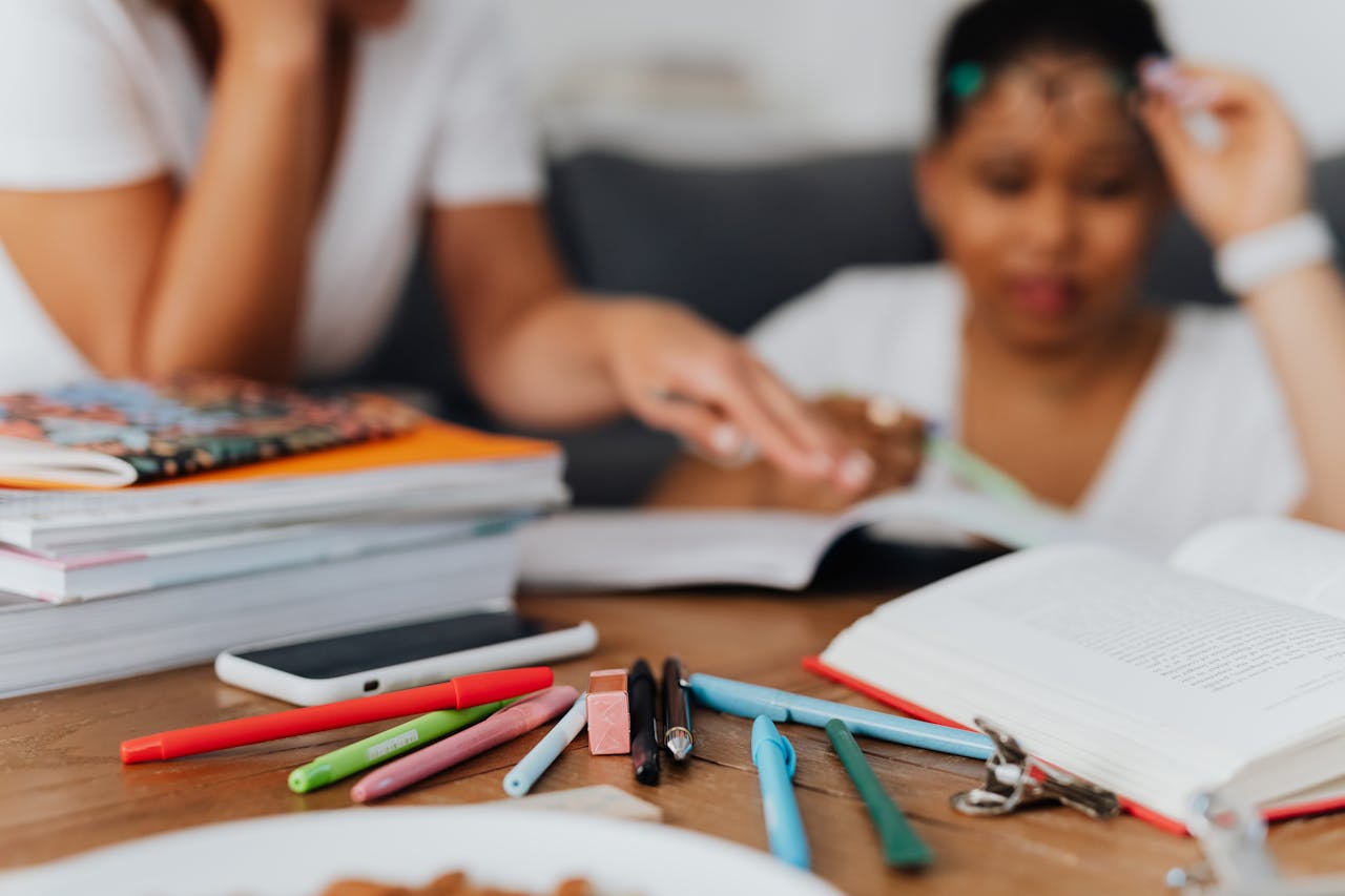 A mother and child studying with books and stationery at a wooden table.
