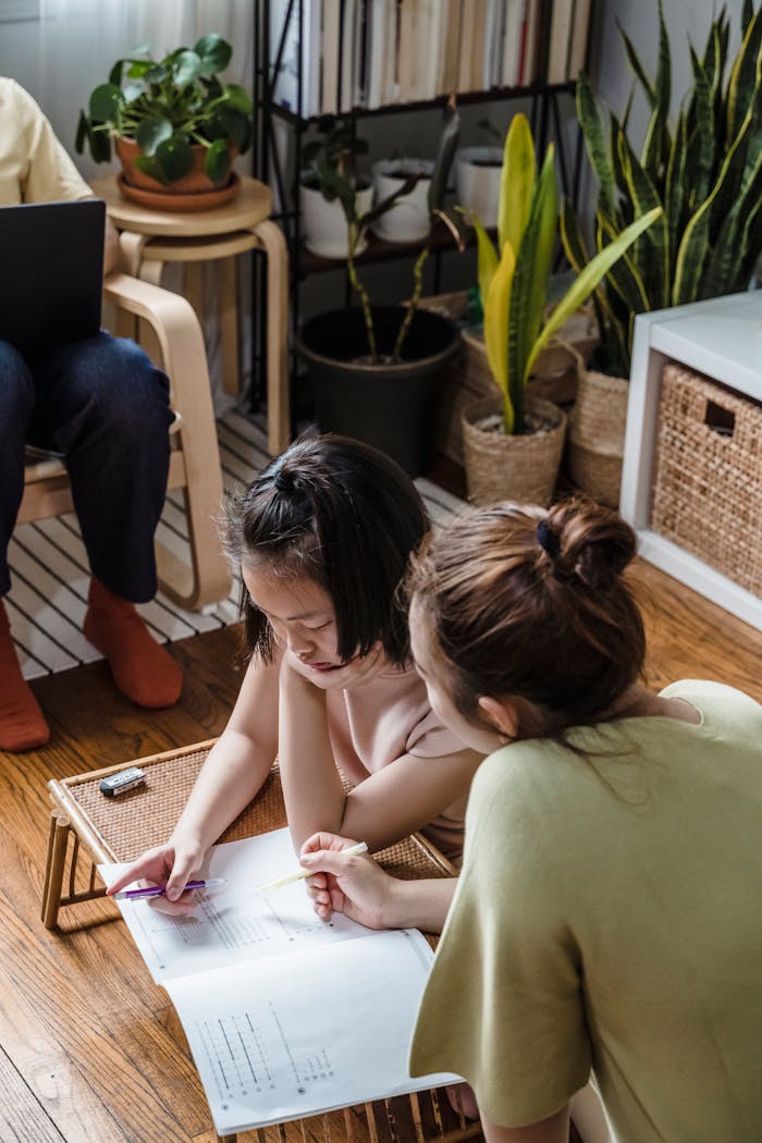 A mother assists her daughter with schoolwork in a cozy living room setting.