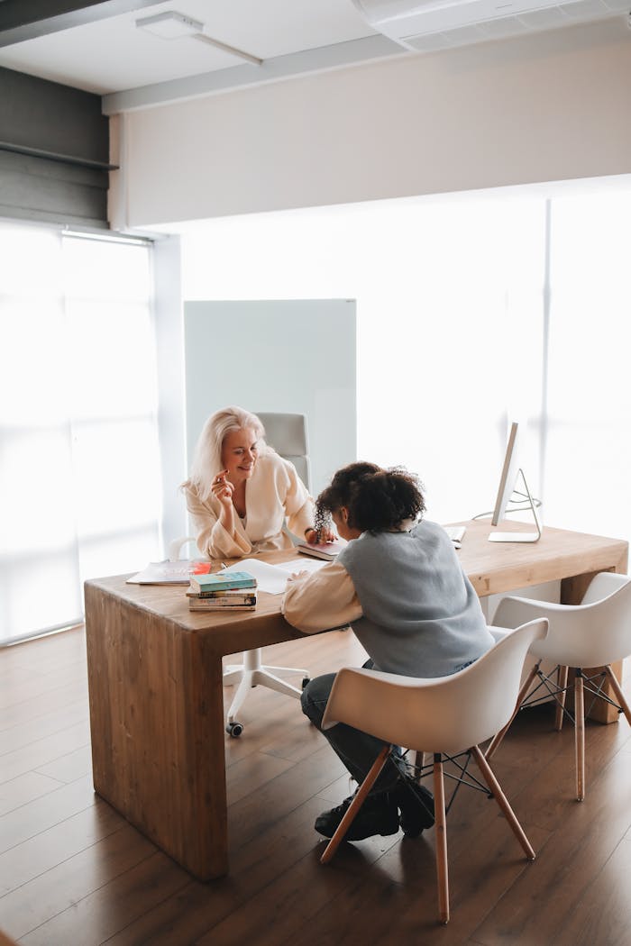 Two women engaged in a learning session at a wooden desk in a modern, bright office setting.