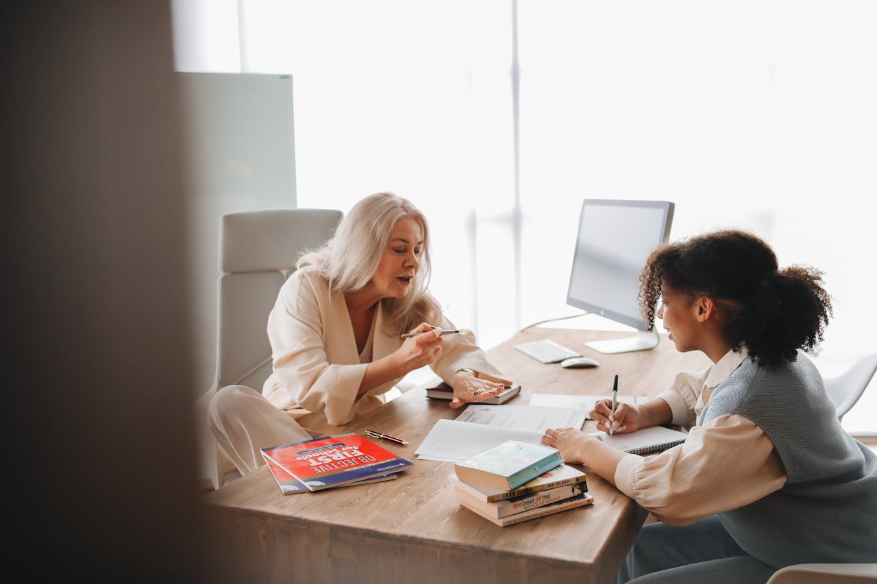 Educator explains concepts to a student in a classroom environment with books and notes.